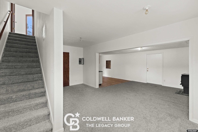 staircase featuring electric panel, carpet flooring, and a wood stove