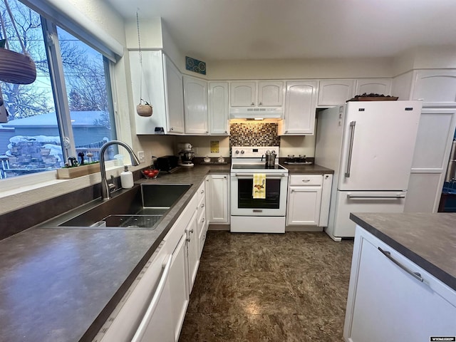 kitchen featuring under cabinet range hood, a sink, dark countertops, white cabinetry, and white appliances