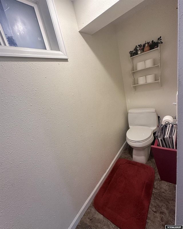 bathroom with baseboards, toilet, and a textured wall