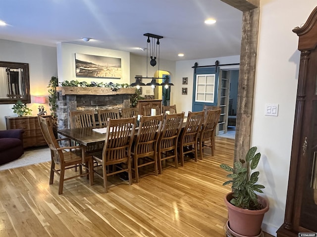 dining room featuring a fireplace, a barn door, recessed lighting, and wood finished floors