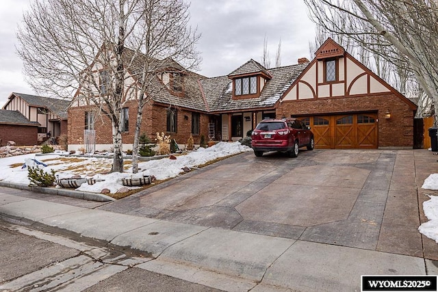 english style home with a garage, brick siding, concrete driveway, and a chimney