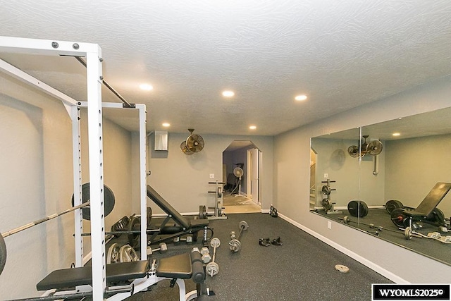 exercise room with arched walkways, recessed lighting, a textured ceiling, and baseboards