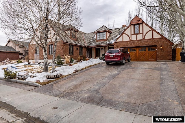 tudor home featuring brick siding, stucco siding, a chimney, a garage, and driveway