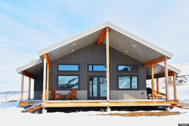 snow covered rear of property featuring a porch, french doors, and board and batten siding