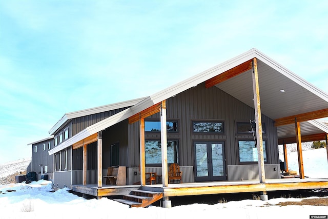 snow covered rear of property featuring covered porch and french doors