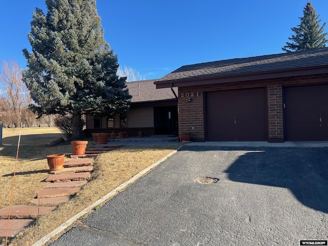 ranch-style home with aphalt driveway, an attached garage, and brick siding