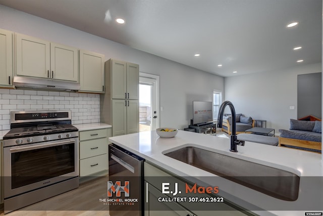 kitchen with under cabinet range hood, a sink, open floor plan, stainless steel appliances, and light countertops