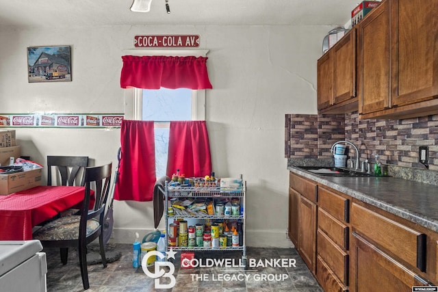 kitchen with a sink, tasteful backsplash, dark countertops, brown cabinetry, and baseboards