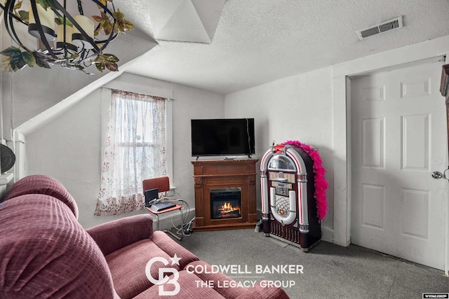 living area with visible vents, a textured ceiling, carpet floors, and a glass covered fireplace