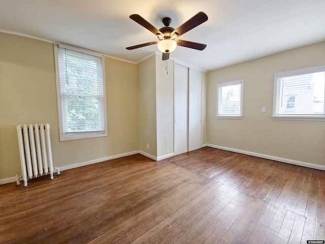 unfurnished room with baseboards, radiator heating unit, ceiling fan, and hardwood / wood-style floors