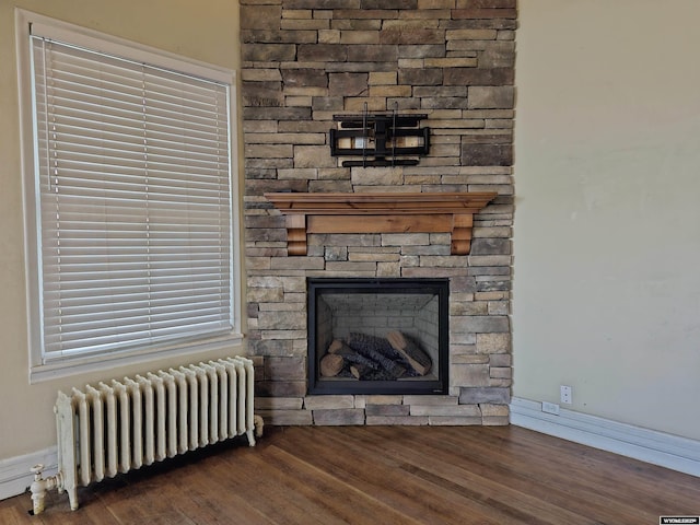 interior details featuring a stone fireplace, radiator, baseboards, and wood finished floors