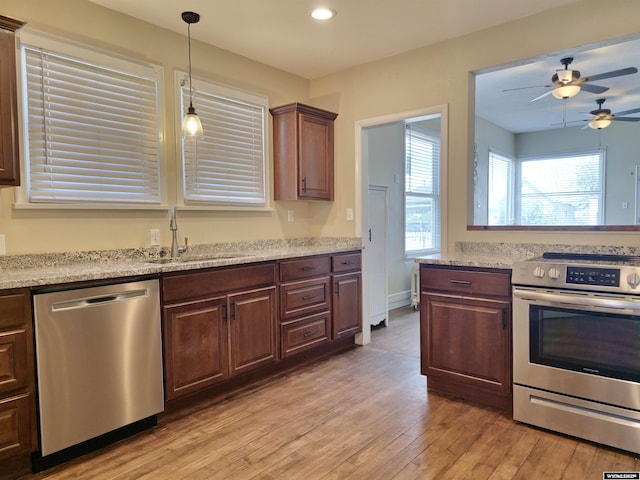 kitchen featuring decorative light fixtures, light wood-style flooring, stainless steel appliances, a ceiling fan, and a sink