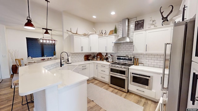 kitchen featuring light wood-style flooring, a sink, appliances with stainless steel finishes, a peninsula, and wall chimney range hood