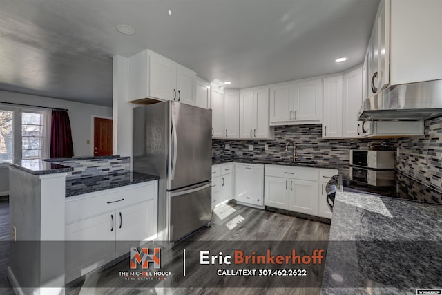 kitchen with under cabinet range hood, a peninsula, freestanding refrigerator, white dishwasher, and a sink