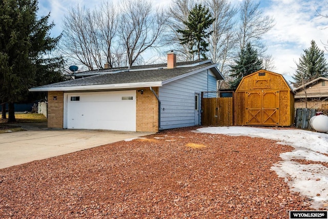 view of property exterior with an outbuilding, fence, a garage, brick siding, and a chimney