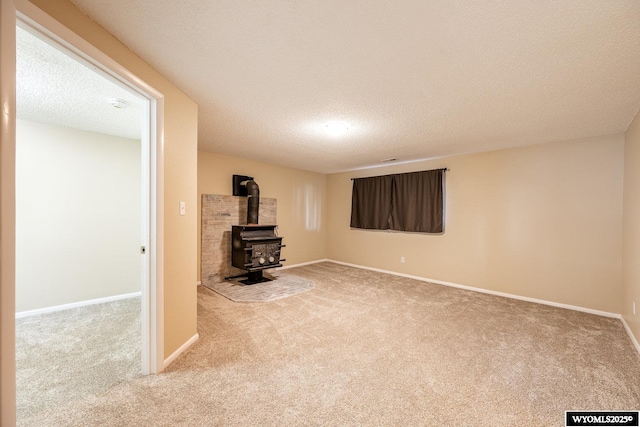 unfurnished living room with baseboards, carpet floors, a textured ceiling, and a wood stove