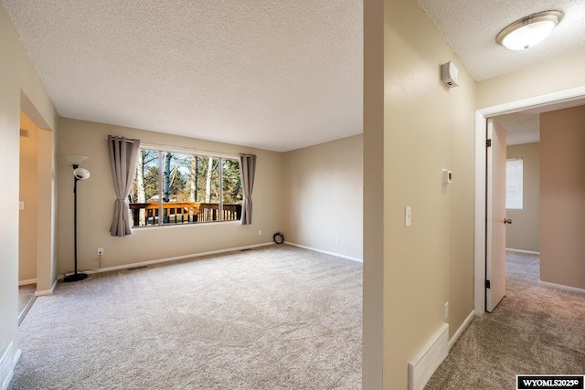 spare room featuring a textured ceiling, carpet, visible vents, and baseboards