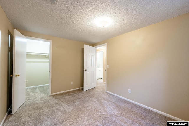 unfurnished bedroom with a textured ceiling, baseboards, a walk in closet, and carpet