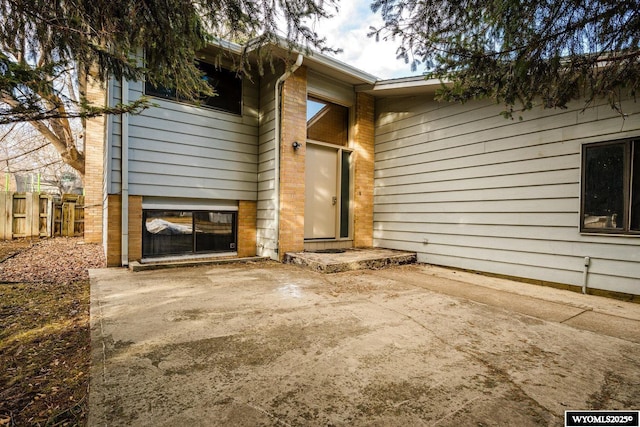 view of exterior entry with a patio area, brick siding, and fence