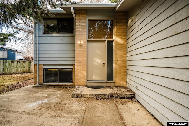 view of exterior entry featuring fence and brick siding