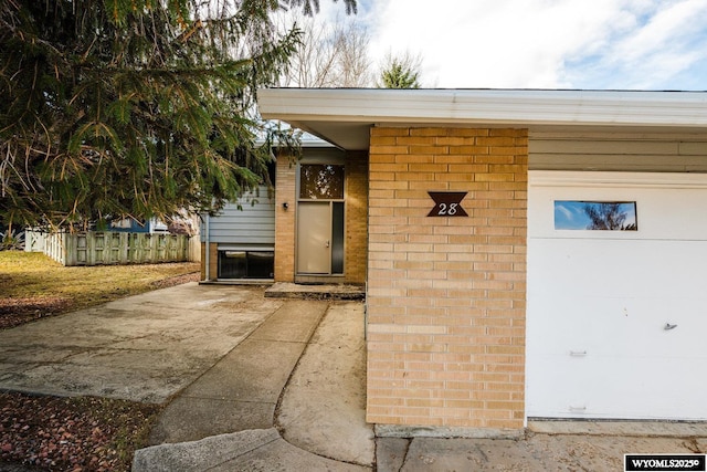 view of exterior entry featuring fence and brick siding