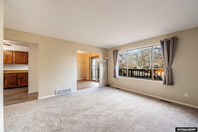 carpeted empty room featuring baseboards, visible vents, and a textured ceiling