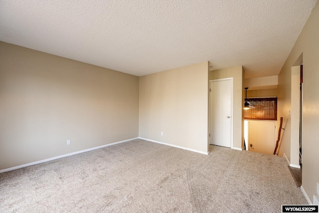 empty room with carpet flooring, baseboards, and a textured ceiling