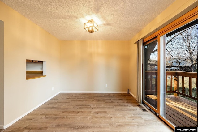 unfurnished room featuring a textured ceiling, wood finished floors, visible vents, and baseboards