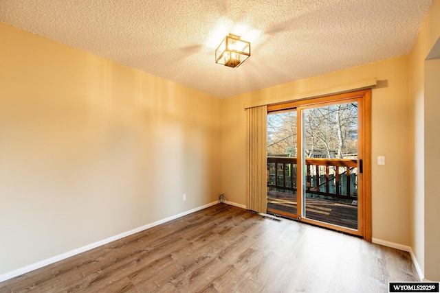 spare room with a textured ceiling, wood finished floors, visible vents, and baseboards