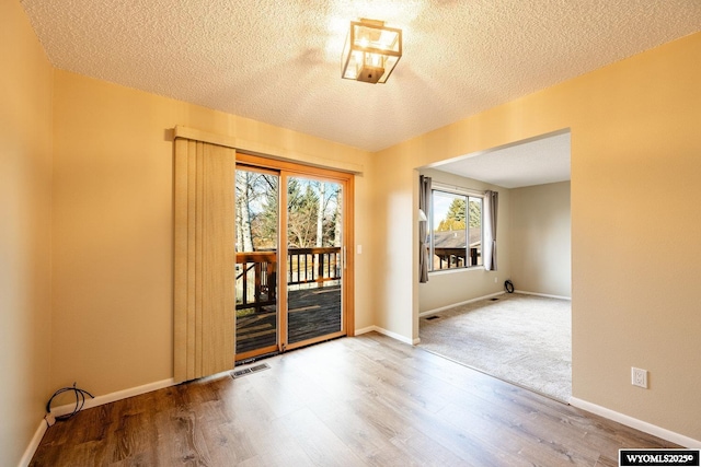 spare room with visible vents, baseboards, a textured ceiling, and wood finished floors