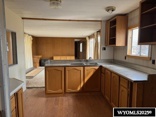 kitchen featuring open shelves, wood finished floors, a peninsula, and a sink