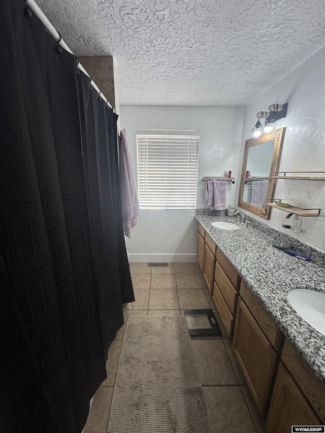 bathroom with a sink, a textured ceiling, double vanity, and tile patterned flooring