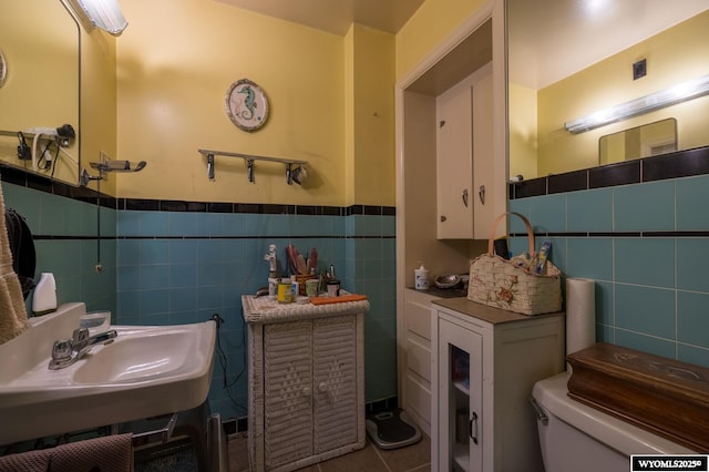 half bathroom with a wainscoted wall, toilet, a sink, tile walls, and tile patterned flooring
