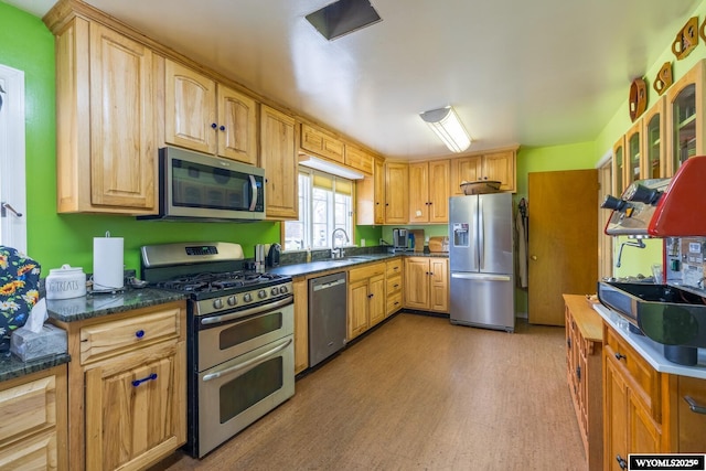 kitchen featuring light wood-style flooring, a sink, glass insert cabinets, appliances with stainless steel finishes, and dark countertops