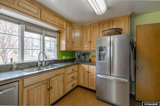 kitchen with dark stone countertops, appliances with stainless steel finishes, wood finished floors, and a sink
