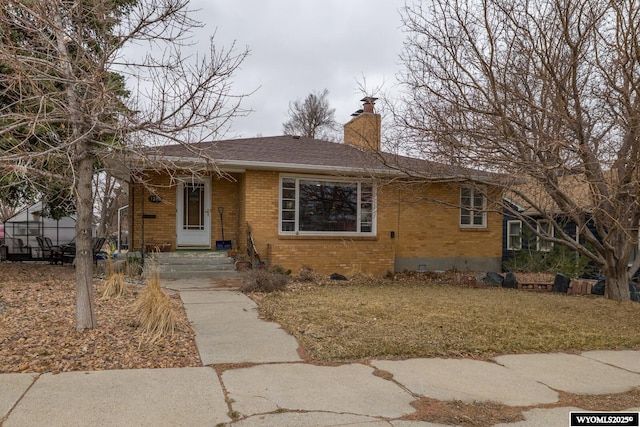 bungalow-style home with a front lawn, a shingled roof, crawl space, brick siding, and a chimney