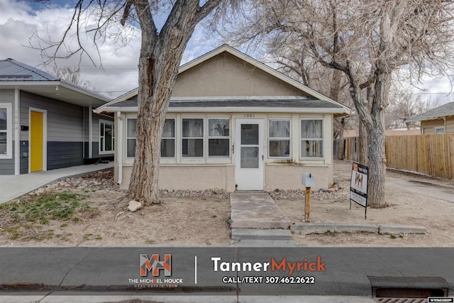 bungalow-style home with stucco siding and fence