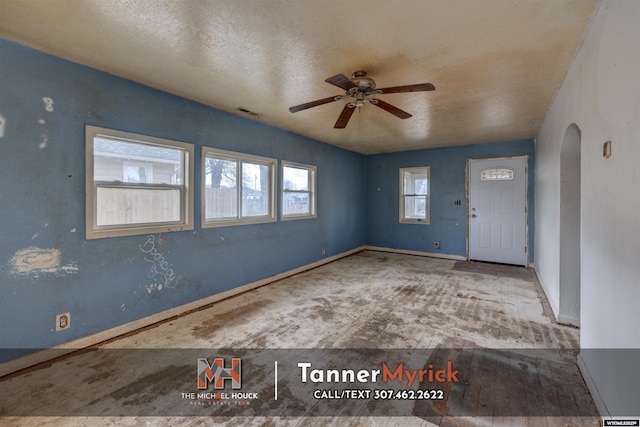foyer entrance featuring visible vents, baseboards, ceiling fan, arched walkways, and a textured ceiling