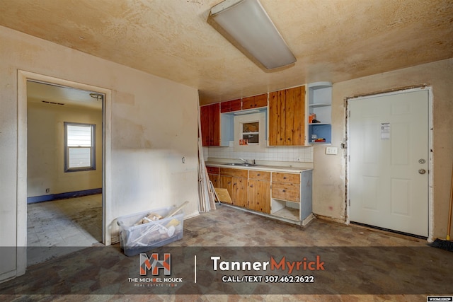 kitchen with a sink, open shelves, backsplash, light countertops, and baseboards