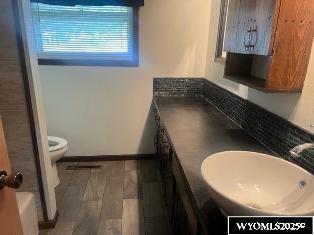 full bathroom with toilet, baseboards, a sink, double vanity, and wood finished floors
