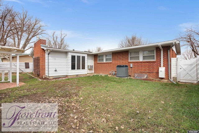 rear view of property featuring a chimney, cooling unit, fence, brick siding, and a lawn