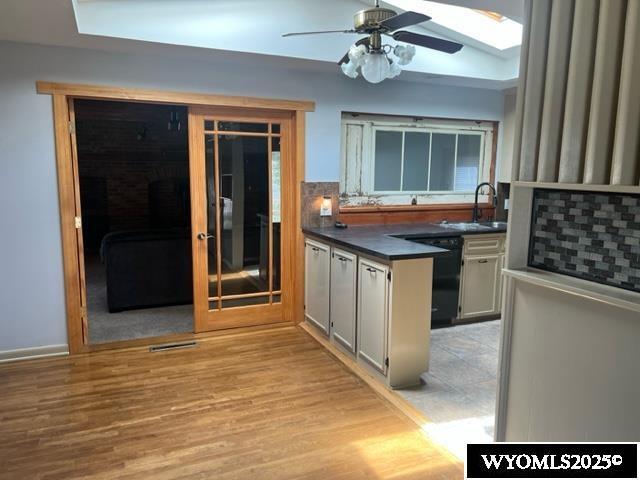 kitchen featuring a sink, a ceiling fan, light wood finished floors, dishwasher, and dark countertops