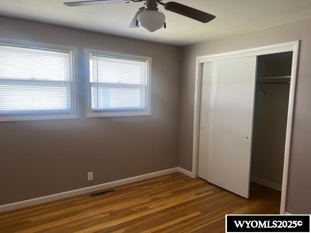 unfurnished bedroom featuring baseboards, visible vents, a ceiling fan, a closet, and wood finished floors