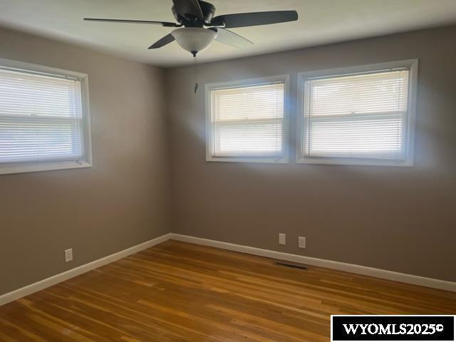 unfurnished room with baseboards, visible vents, ceiling fan, and wood finished floors