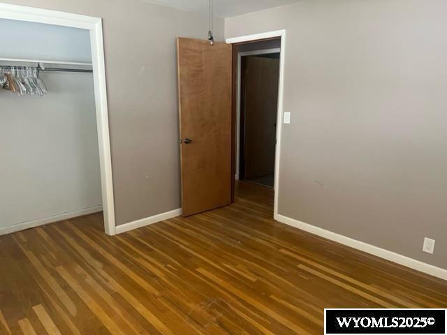 unfurnished bedroom with baseboards, wood finished floors, and a closet