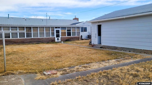 back of property featuring brick siding, a chimney, a lawn, and a sunroom