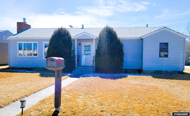 view of front of home with a front yard, roof with shingles, and a chimney