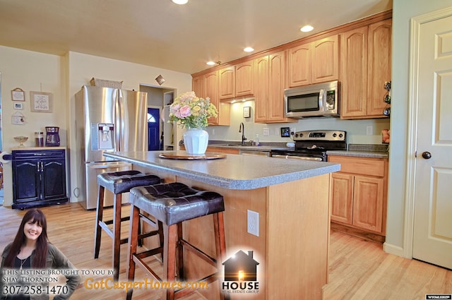 kitchen with a breakfast bar, a center island, appliances with stainless steel finishes, and light brown cabinetry