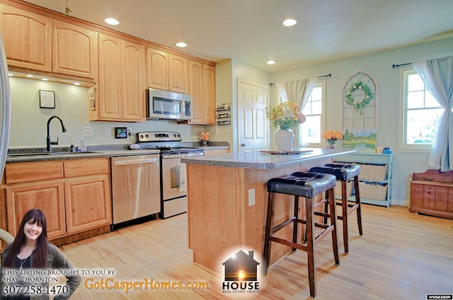 kitchen with a breakfast bar, a sink, light brown cabinetry, stainless steel appliances, and a center island