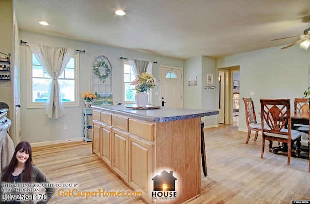 kitchen featuring a breakfast bar area, a ceiling fan, a kitchen island, light brown cabinetry, and light wood-type flooring